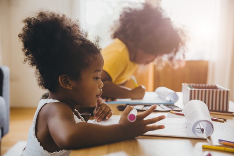 American Black preschool daughter kids doing homework learning education with her sister living together at home.