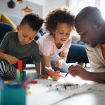 Portrait of father with two small children drawing pictures at home, multi ethnic family and home schooling.