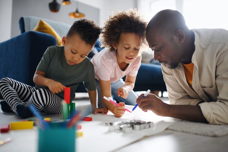Portrait of father with two small children drawing pictures at home, multi ethnic family and home schooling.