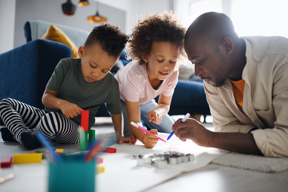 Portrait of father with two small children drawing pictures at home, multi ethnic family and home schooling.