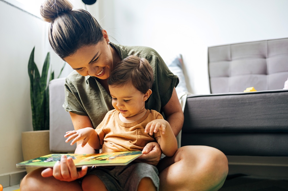 Mom reading a book with baby boy at home. Early age children education, development. Mother and child spending time together. Candid lifestyle.